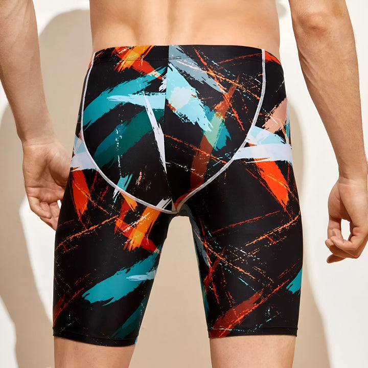 Homme portant un jammer de natation noir avec des motifs abstraits orange, turquoise et blanc. Vêtement de sport moulant, idéal pour la compétition.
