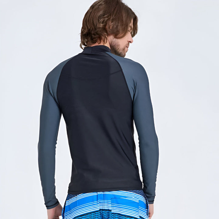 Homme portant un rashguard de bain noir et gris à manches longues et un short de bain bleu avec des rayures blanches.