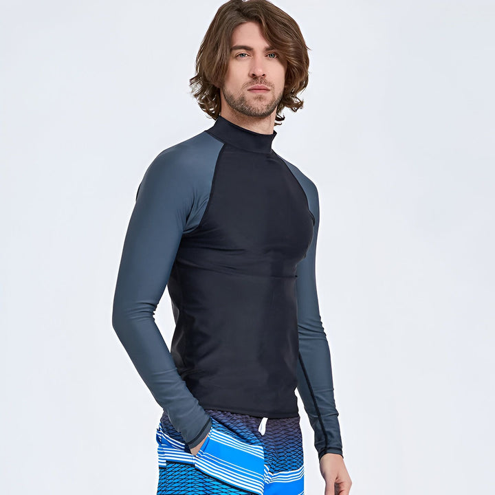 Homme portant un rashguard de bain noir à manches longues et un short de bain à motifs. Vêtement de protection solaire pour la plage ou la piscine. Mode masculine pour l'été.
