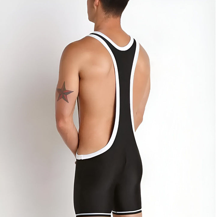 Un homme en justaucorps de lutte noir et blanc, posant avec sa main derrière sa tête. Il a une expression sérieuse. Le justaucorps est moulant et met en valeur sa musculature.