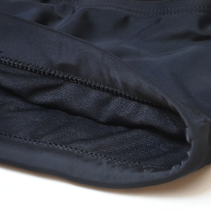 Torse d'homme bronzé en maillot de bain noir, vue de profil. Silhouette athlétique et musclée. Détail sur les abdominaux et la ceinture du slip de bain. Fond blanc uni.