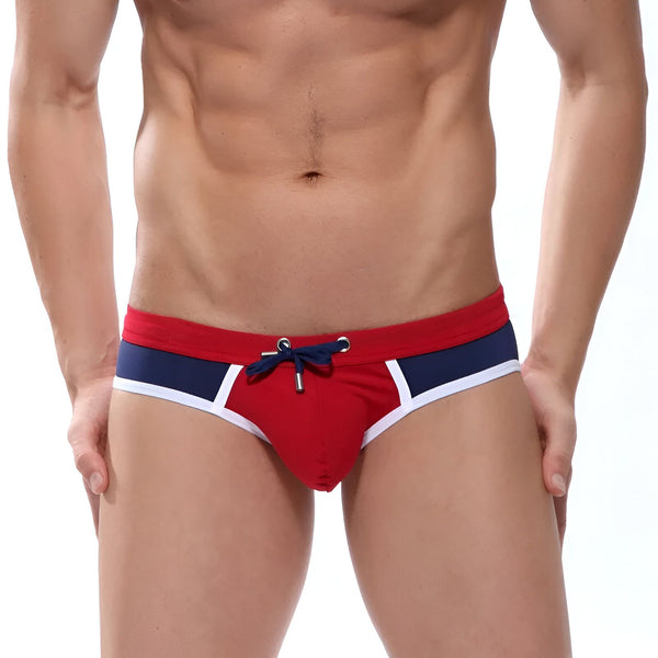 Un homme torse nu, portant un slip de bain rouge, bleu et blanc. Idéal pour la plage ou la piscine. Mode masculine, style estival, maillot de bain homme.