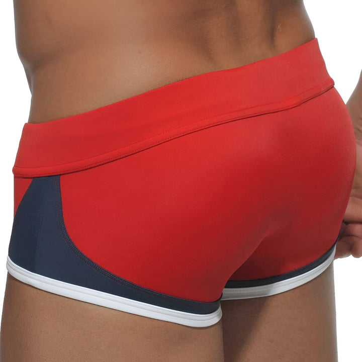 Homme en slip de bain bleu marine avec détails colorés (jaune, orange, blanc). Cordon jaune à la taille. Vue rapprochée du torse et des hanches. Idéal pour la plage ou la piscine.