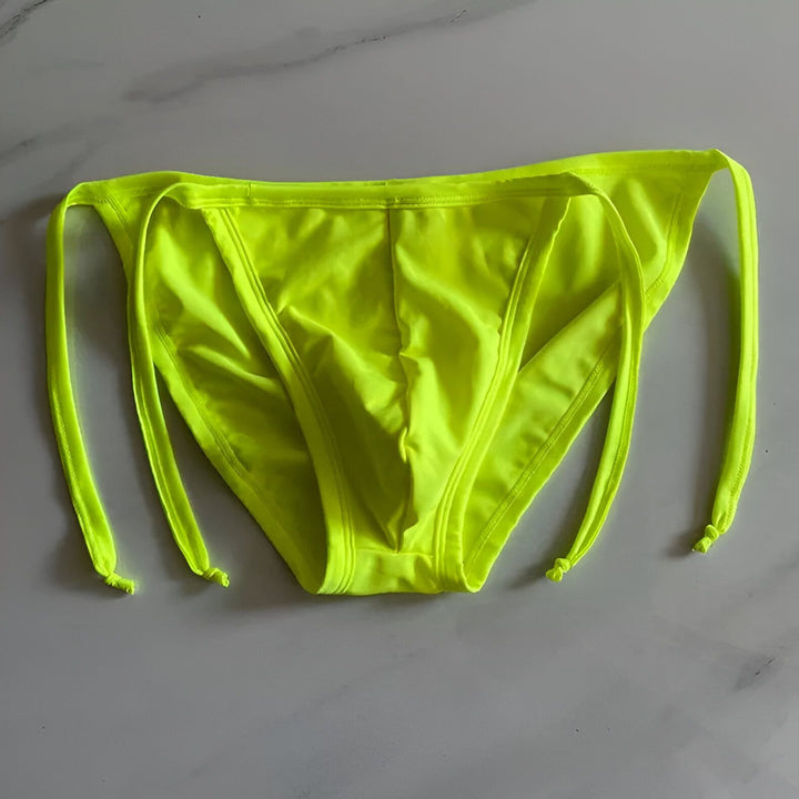 Homme musclé portant un slip de bain jaune fluo avec des cordons à nouer sur le côté. Gros plan sur les abdominaux et le maillot de bain.