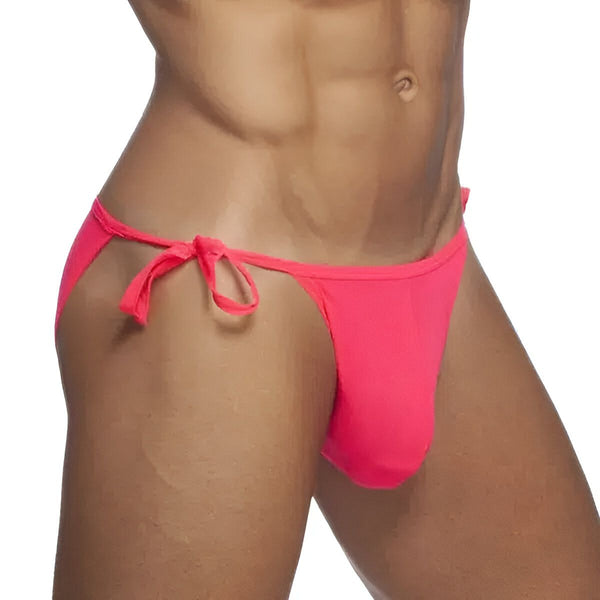 Image d'un homme musclé portant un slip de bain rose vif avec des cordons sur les côtés. Le slip est très échancré et laisse apparaître une grande partie de la peau. L'homme a un bronzage prononcé.