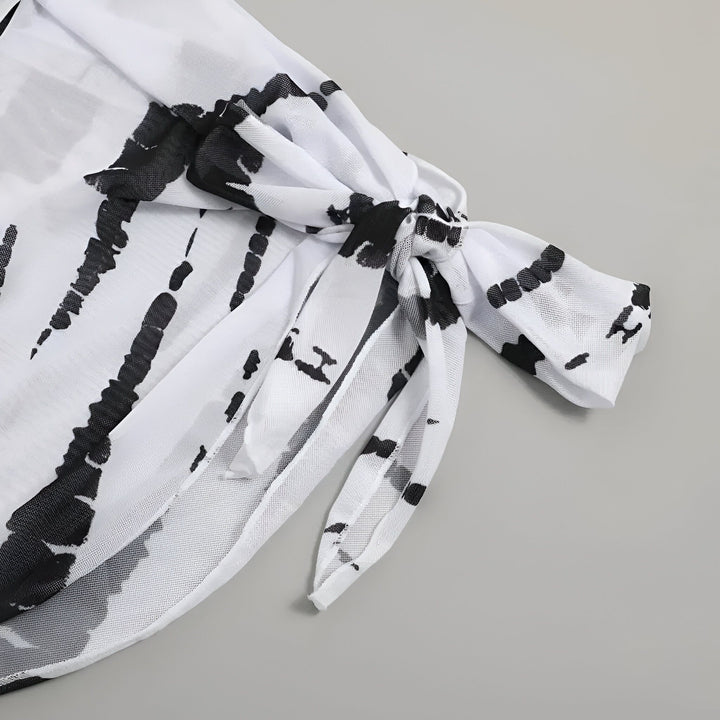 Gros plan d'un paréo blanc à motifs tie-dye noirs, noué. Idéal pour la plage ou la piscine. Accessoire de mode estival, léger et tendance.