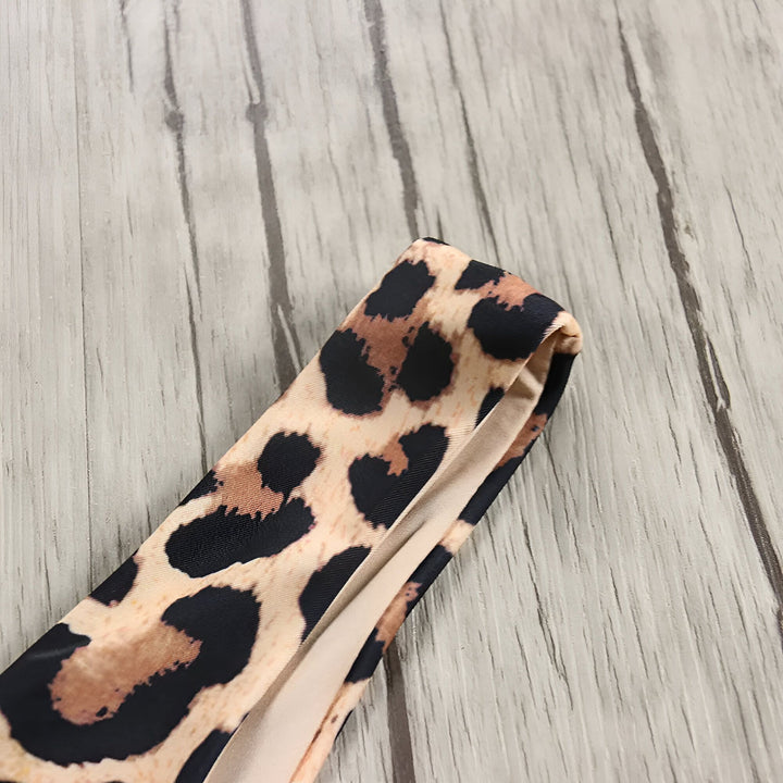 Image rapprochée d'un bas de bikini imprimé léopard sur un fond en bois clair. Détails de la texture du tissu et de l'imprimé animalier. Idéal pour la mode estivale, les maillots de bain et les tendances actuelles.