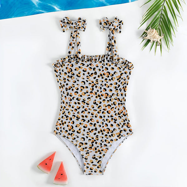 Maillot de bain une pièce pour enfant avec motif léopard, bretelles à nouer, fond blanc. Idéal pour la plage ou la piscine.
