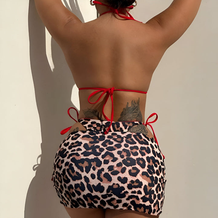 Femme portant un bikini léopard avec des liens rouges. Elle a des tatouages sur son corps et un piercing au nombril.