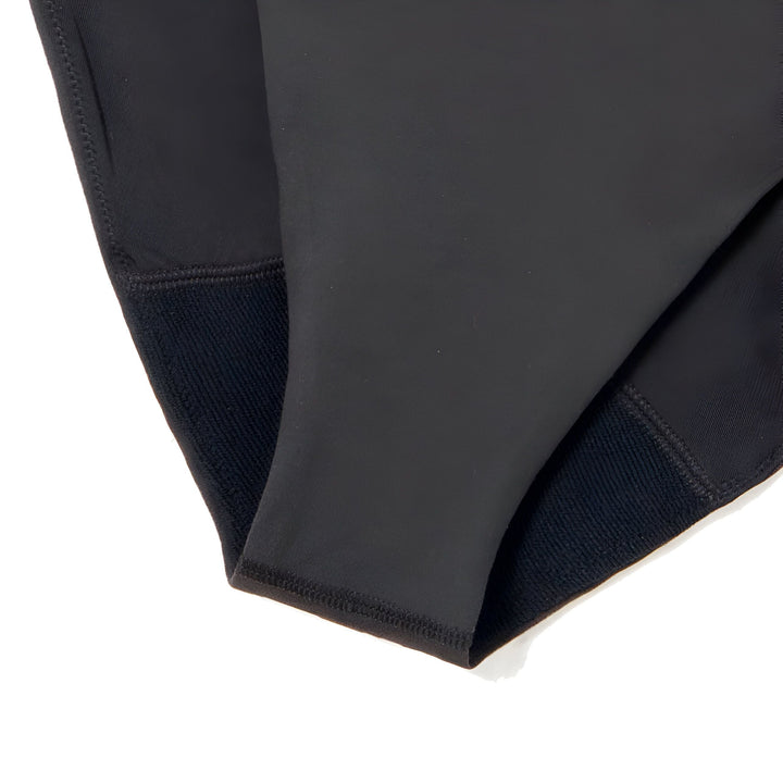 Femme blonde en maillot de bain noir une pièce, posant près d'une piscine. Cactus et verdure en arrière-plan. Tatouages sur le bras. Mode été, style de vie.