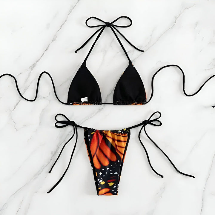 Une femme porte un bikini avec un motif d'aile de papillon monarque. Le bikini est orange, jaune et noir. Le fond est bleu clair.