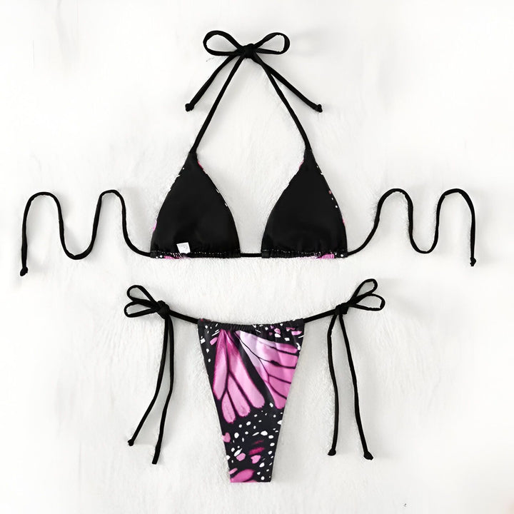 Gros plan d'une femme portant un string noir à motif de papillon monarque. Bikini à ficelles noires, peau bronzée, abdomen visible. Arrière-plan flou de l'océan. Mode estivale, maillot de bain tendance.