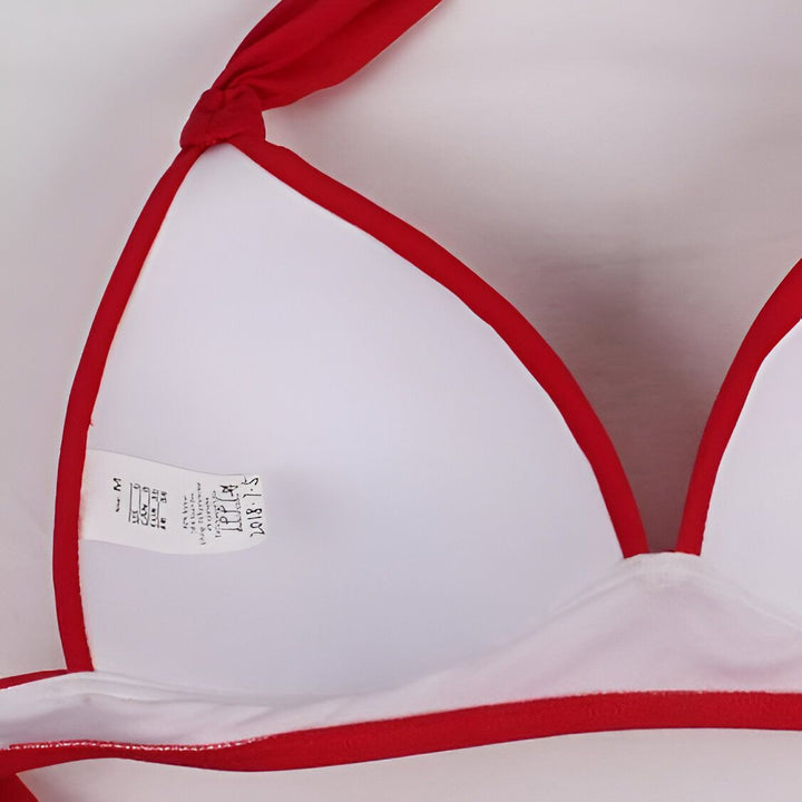 Vue rapprochée d'un haut de bikini blanc avec des bordures rouges, l'intérieur du bikini visible avec une étiquette de taille et des notes manuscrites. Idéal pour la plage, la piscine et les vacances d'été.