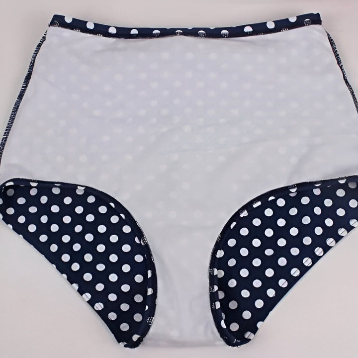 Maillot de bain deux pièces style rétro. Haut rouge à nouer dans le cou et dans le dos, culotte taille haute bleu marine à pois blancs avec une ceinture rouge.