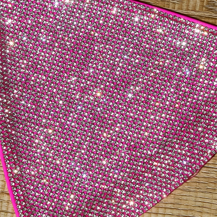 Gros plan d'un tissu rose fuchsia orné de strass scintillants, disposés en motif régulier. Texture brillante et luxueuse.