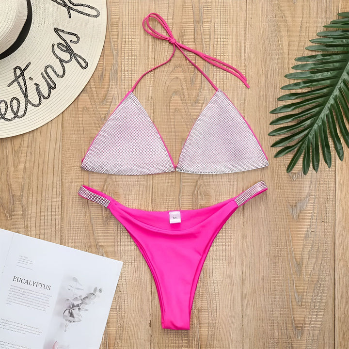 Femme en bikini rose vif et argenté scintillant. Haut de bikini triangulaire à paillettes argentées et bas assorti. La femme est devant un lavabo blanc dans une salle de bain.