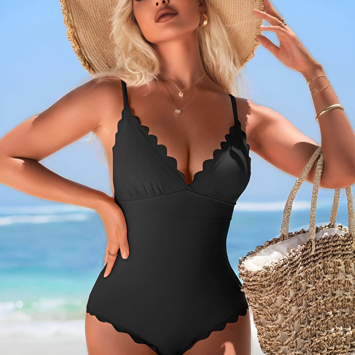 Femme blonde portant un maillot de bain noir une pièce avec des détails festonnés à la plage.