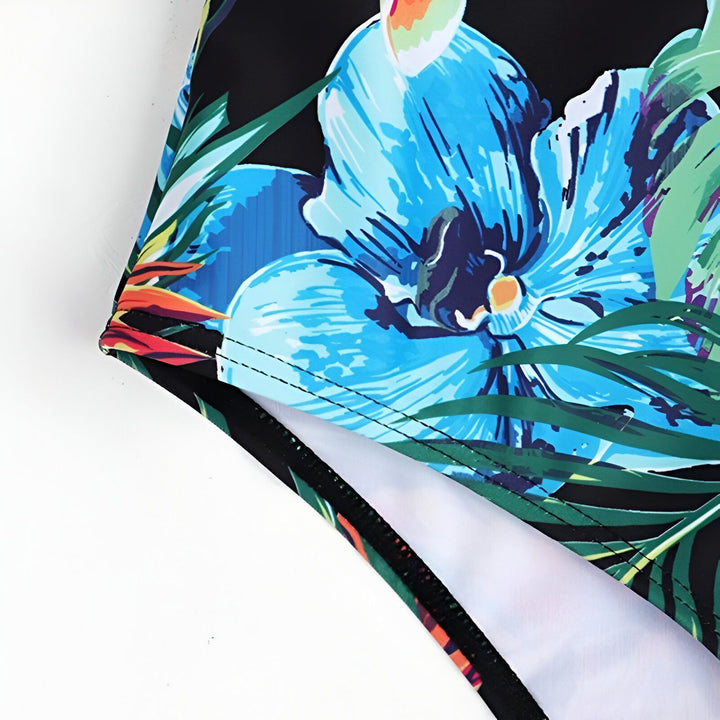 Maillot de bain une pièce imprimé floral tropical vibrant, avec un haut bandeau noir élégant et des bretelles fines. Le design présente des découpes graphiques à la taille.
