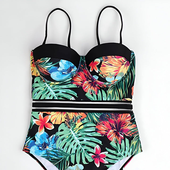 Vue arrière d'une femme portant un maillot de bain une pièce à motifs tropicaux avec des fleurs colorées et des feuilles vertes. Elle porte un bracelet doré ajouré.