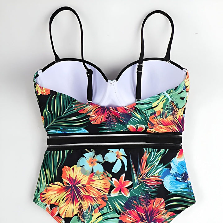Gros plan d'une femme portant un maillot de bain une pièce noir avec un imprimé floral multicolore sur un lit blanc.
