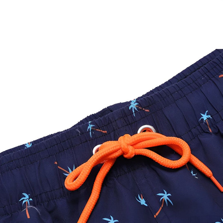 Homme torse nu, portant un short de bain bleu marine à motifs de palmiers.