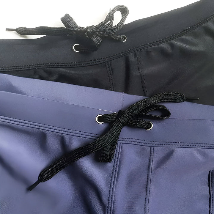 Homme torse nu en short de bain bleu marine. Vue arrière, peau bronzée avec gouttes d'eau. Style plage, été, vacances.