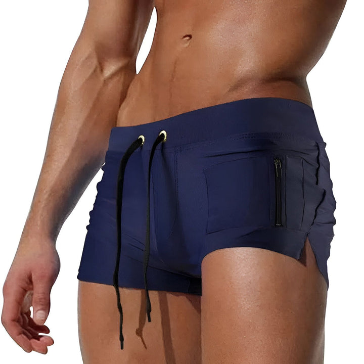 Homme torse nu, portant un short de bain bleu marine avec cordon de serrage et poche. Corps athlétique et musclé. Idéal pour la mode masculine estivale et les vêtements de plage.