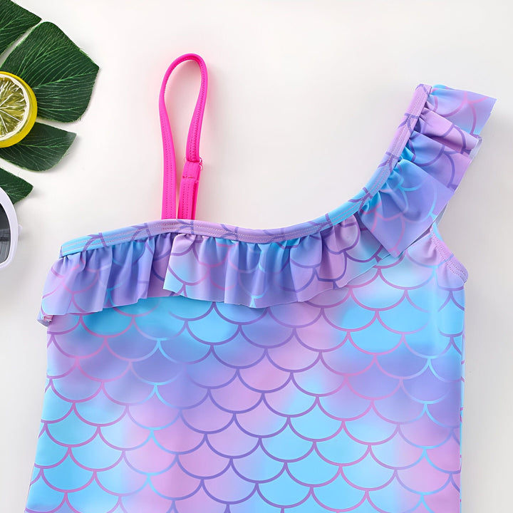 Maillot de bain une pièce pour fille, motif écailles de sirène, volants bleus et roses. Accessoires de plage : coquillages, citron, lunettes de soleil. Idéal pour les vacances d'été à la mer.