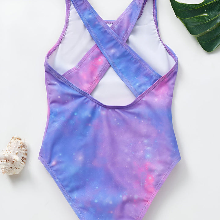 Vue arrière d'un maillot de bain une pièce pour fille avec un motif galaxie violet et rose, bretelles croisées, coquillage et feuille. Idéal pour la natation et la plage.