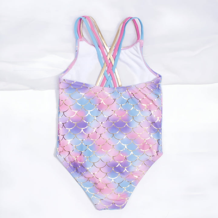 Maillot de bain une pièce pour fille, motif écailles de sirène aux couleurs pastel rose, bleu et violet, orné d'un coquillage à paillettes. Bretelles croisées rose, bleu et dorées. Fond blanc uni.