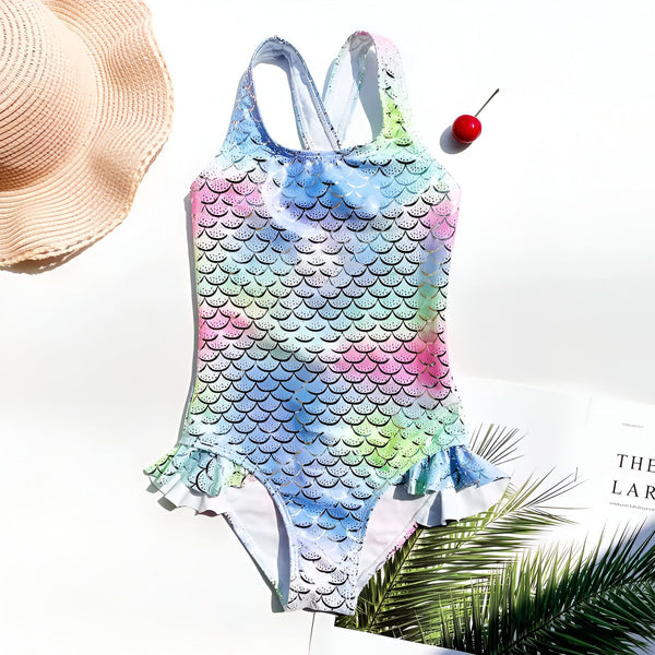 Dos d'un maillot de bain pour enfant avec un motif d'écailles de sirène arc-en-ciel et argentées. Les bretelles croisées ajoutent une touche fantaisie à ce vêtement de bain d'été. Idéal pour la plage ou la piscine.