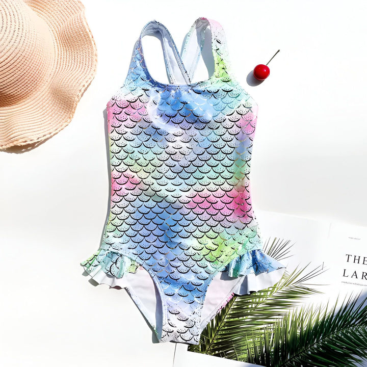 Dos d'un maillot de bain pour enfant avec un motif d'écailles de sirène arc-en-ciel et argentées. Les bretelles croisées ajoutent une touche fantaisie à ce vêtement de bain d'été. Idéal pour la plage ou la piscine.