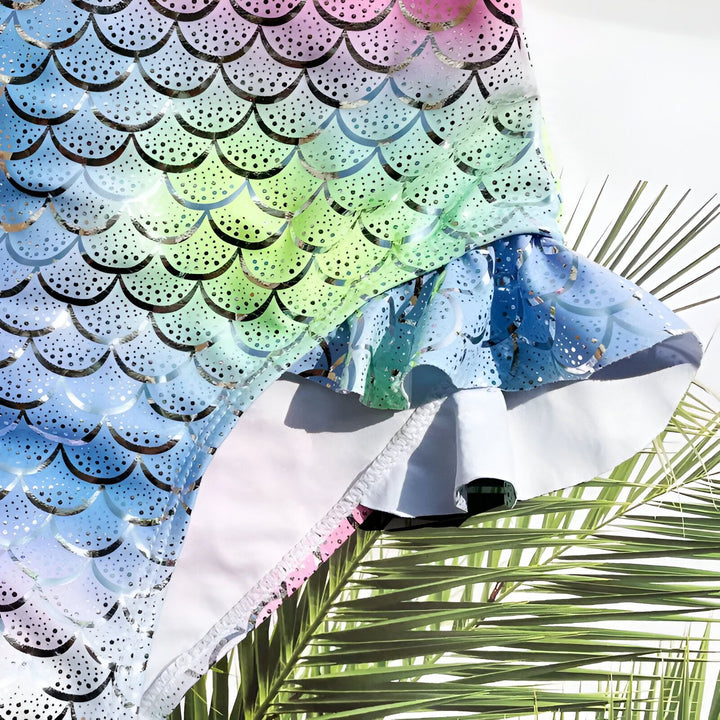 Maillot de bain enfant motif écailles de sirène, tons roses et bleus avec détails brillants argentés. Idéal pour la plage et la piscine.