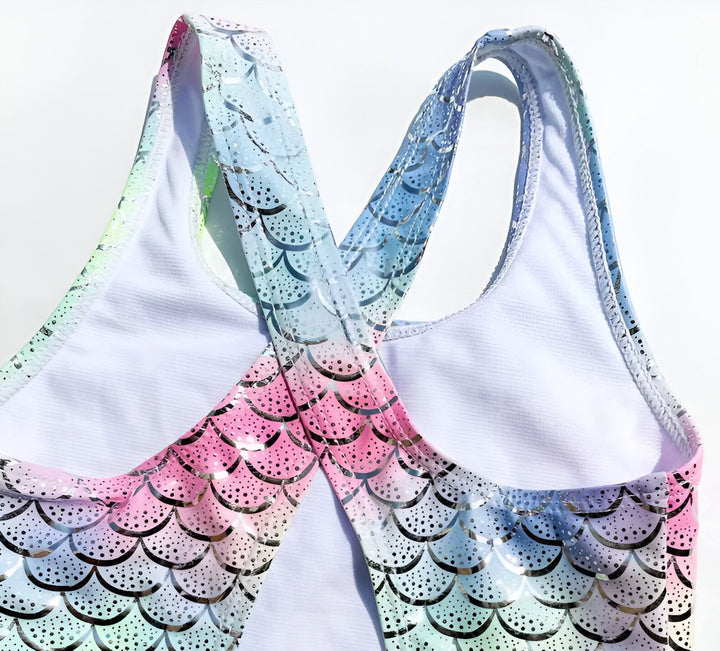 Maillot de bain une pièce pour enfant avec motif écailles de sirène multicolores, accompagné d'un chapeau de paille et d'une cerise, évoquant l'été et les vacances à la plage. Idéal pour les petites nageuses.