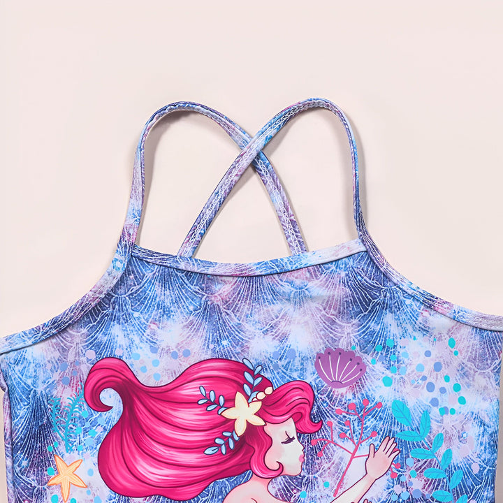 Vue rapprochée du haut d'un maillot de bain pour enfant avec des bretelles croisées. Le maillot est décoré d'un motif représentant une sirène aux cheveux roses dans un décor marin de coquillages, d'étoiles de mer et d'algues. Le fond du maillot évoque des écailles dans des tons de bleu et de violet.