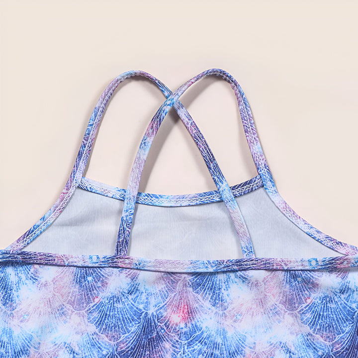 Maillot de bain fille imprimé écailles bleues et violettes, entouré de jouets de plage : étoile de mer, crabe, bouée canard et dauphins rose et bleu. Idéal pour l'été et les vacances.