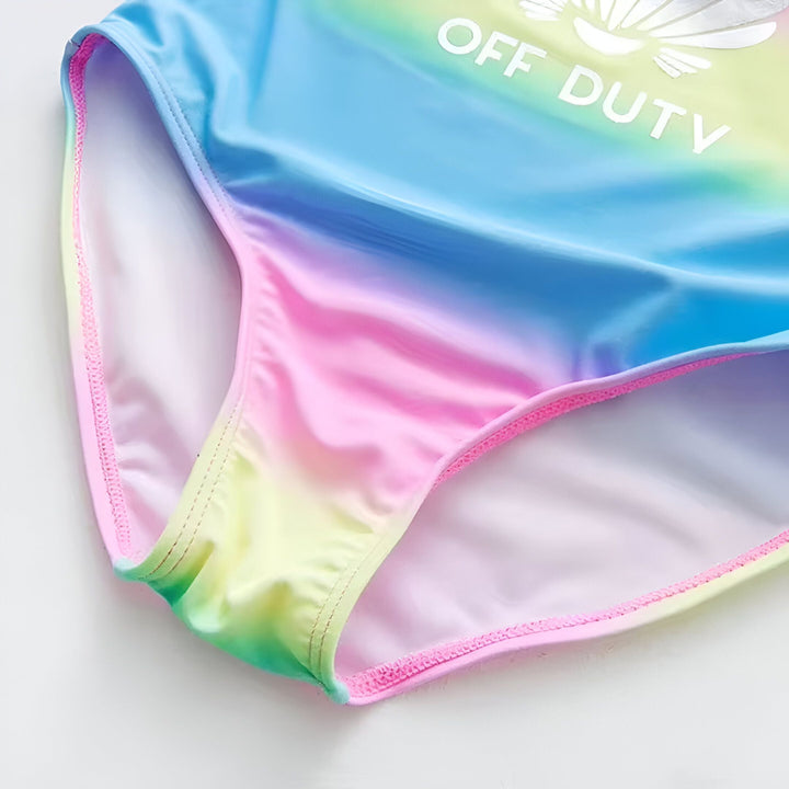 Culotte de maillot de bain arc-en-ciel pour fille avec inscription "OFF DUTY" et motif d'ailes blanches. Détails roses sur les bords.