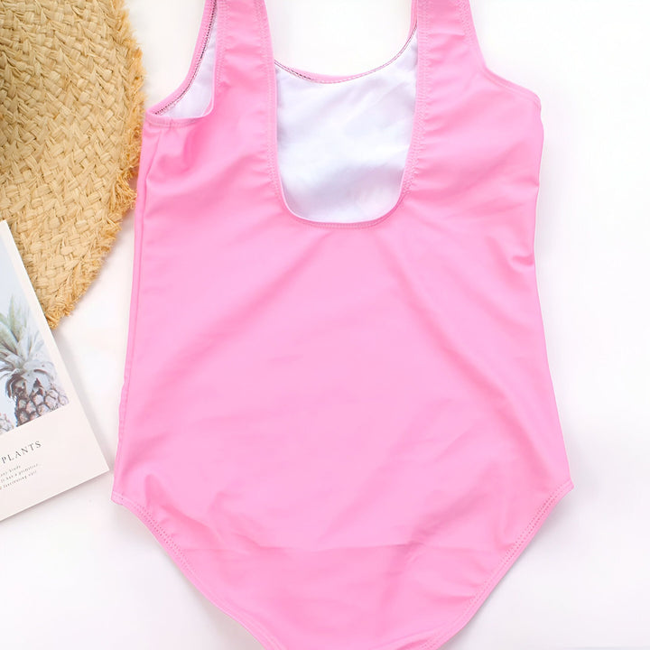 Vue arrière d'un maillot de bain rose pour enfant, posé à plat avec un chapeau de paille et un magazine sur le thème des plantes. Parfait pour les vacances à la plage.
