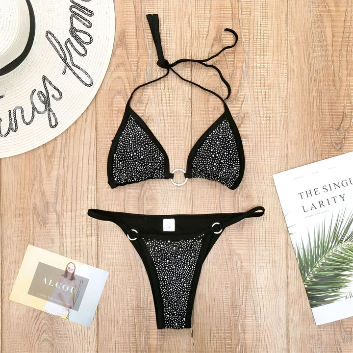 Gros plan d'un bikini noir orné de strass brillants et d'un anneau décoratif. Texture boisée en arrière-plan. Détail luxueux et élégant pour l'été.