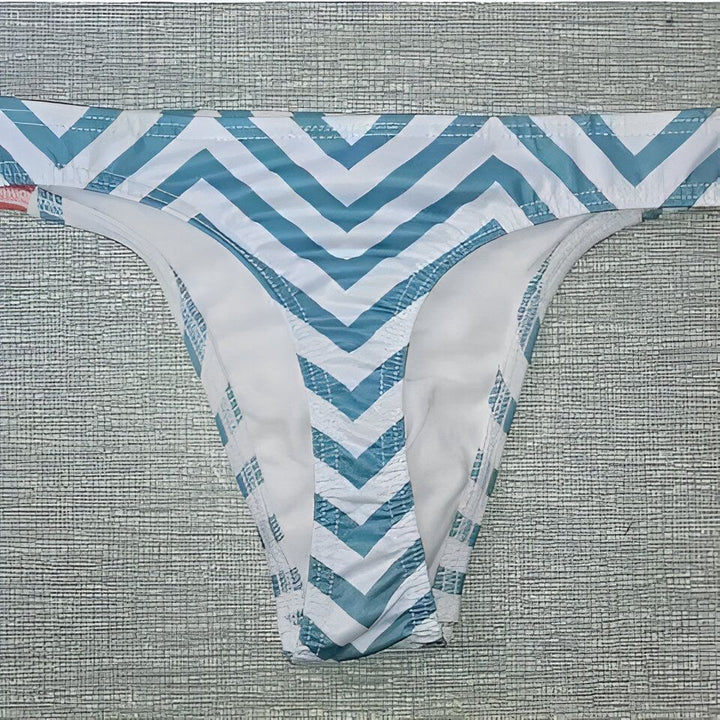 Homme torse nu, portant un string orange avec motif floral. On voit un insert en mousse pour améliorer le galbe. Idéal pour la plage ou la piscine.