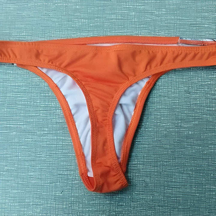 Homme musclé portant un string rayé bleu et blanc avec une ceinture orange, plus un coussinet de contour.