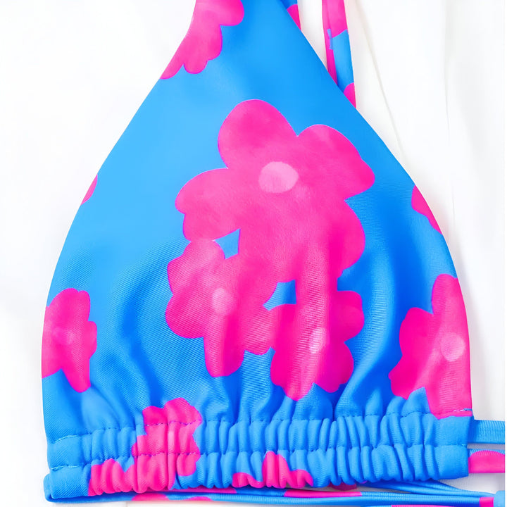 Vue arrière d'une femme portant un bikini à motifs bleu et rose, avec des lanières à nouer dans le dos et sur les côtés du bas. Elle se tient près d'un mur blanc et d'un palmier.