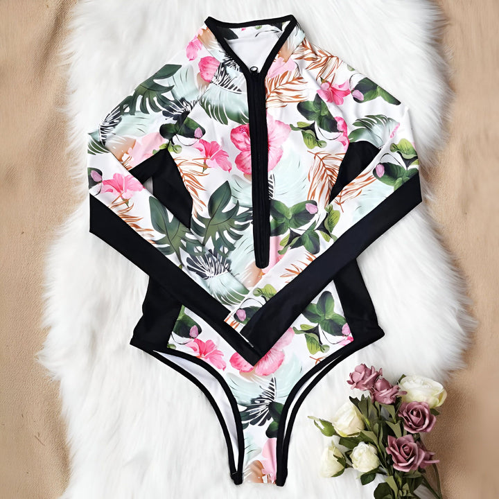 Jeune femme souriante, en maillot de bain floral noir, portant une planche de surf sur la tête à la plage. Mer turquoise en arrière-plan. Idéale pour le surf, l'été, les vacances et l'aventure.