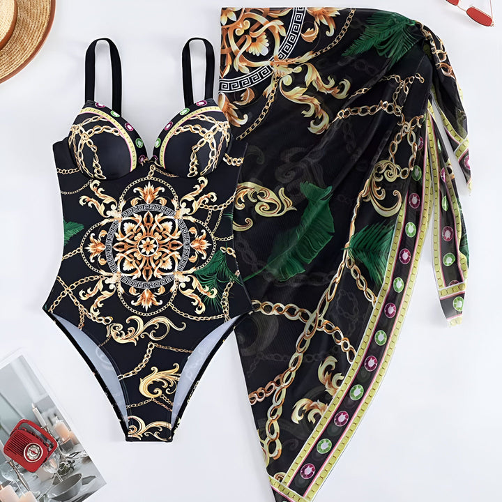 Femme souriante portant un maillot de bain une pièce noir imprimé chaîne dorée avec un paréo assorti noué à la taille. Cheveux bruns ondulés et bijoux discrets.