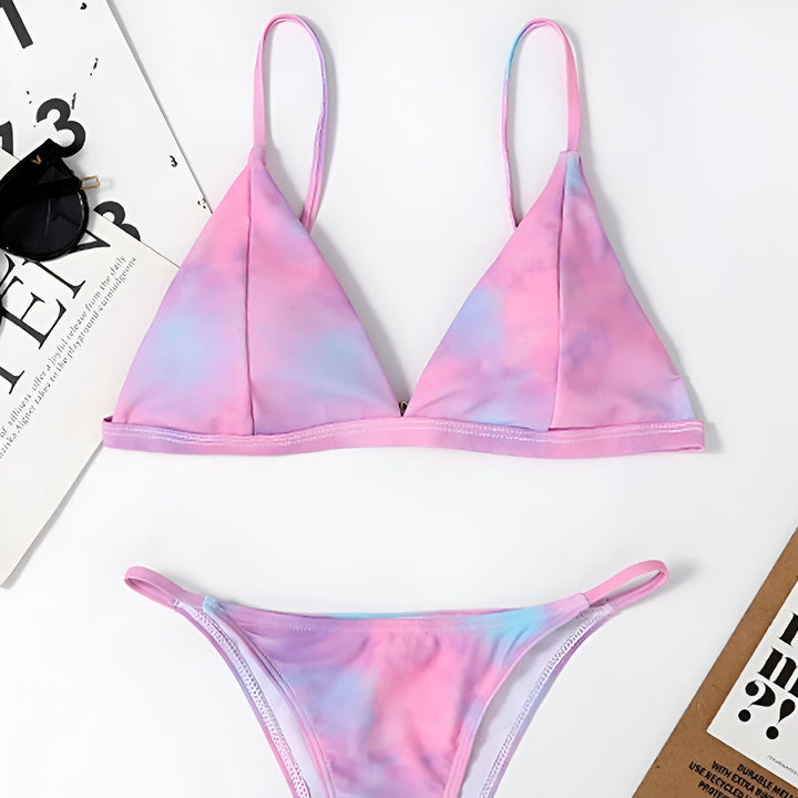 Femme portant un bikini bleu ciel et blanc, motif nuages. Haut triangulaire et bas échancré. Cheveux blonds longs et ondulés.