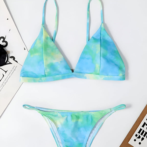 Une femme bronzée porte un bikini à motif nuage bleu et blanc. Vue de face, le bikini met en valeur sa silhouette. Le fond blanc uni crée un contraste net. Parfait pour l'été et la plage.