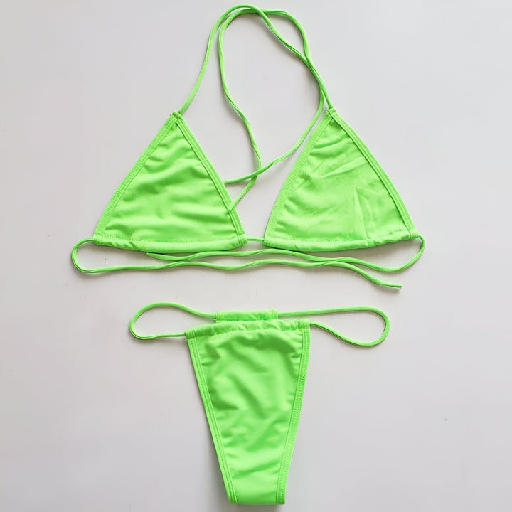 Jeune femme portant un bikini vert fluo et des lunettes de soleil oversize. Elle pose devant un mur rocheux. Mode été, vacances, plage.