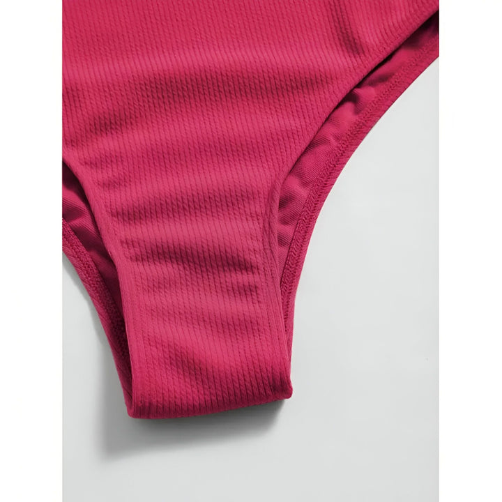 Image d'une femme portant un maillot de bain une pièce asymétrique blanc et bleu clair. Elle porte un collier avec un pendentif et une montre. Le maillot est texturé et met en valeur une silhouette élégante.