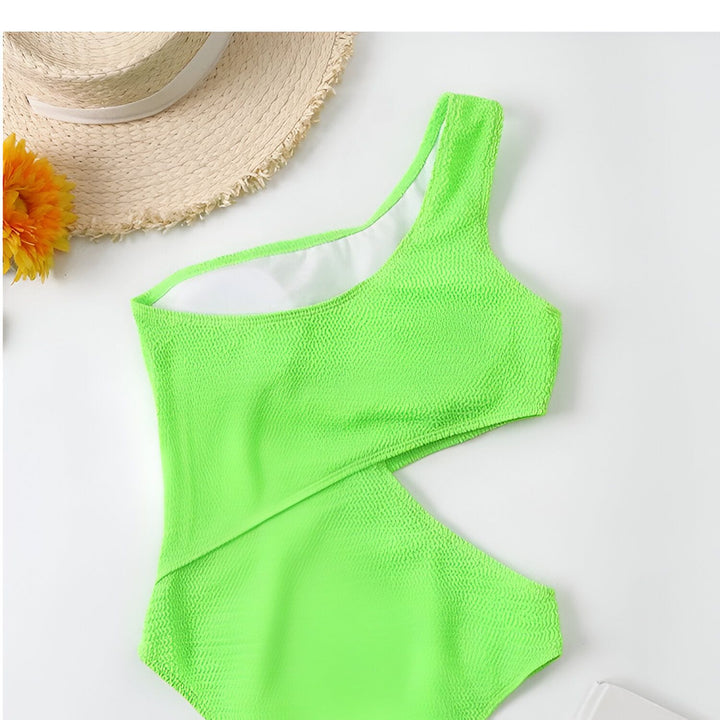 Maillot de bain une pièce lilas texturé avec une épaule, chapeau de paille et fleur jaune sur fond blanc. Vêtement de plage estival pour femme.