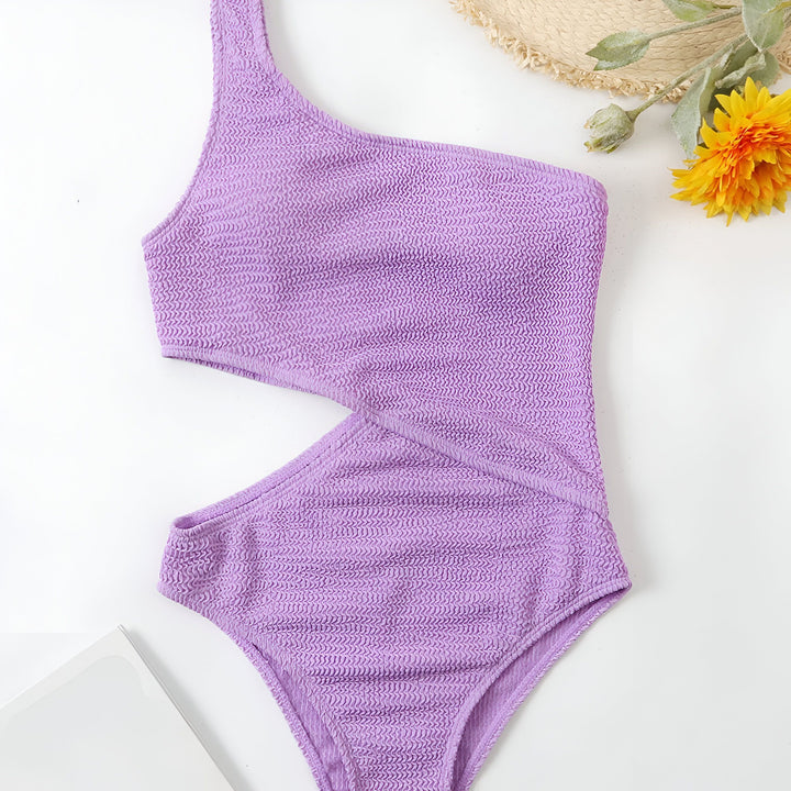 Vue arrière d'une femme portant un maillot de bain une pièce violet texturé avec une épaule dénudée et une découpe latérale, mettant en valeur son dos et sa silhouette.